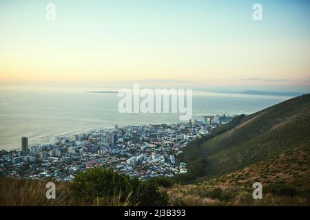 Blick über die Welt. Aufnahme des Blickes auf eine Stadt am Meer von einem Berggipfel. Stockfoto