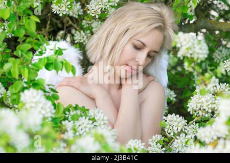 Schöne weibliche Frau mit weißen Flügeln mit weißen Frühlingsblumen. Stockfoto