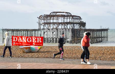 Brighton UK 7. April 2022 - Läufer und Wanderer passieren an einem stürmischen Tag nach einer Nacht mit starken Winden und Regen entlang der Südküste den West Pier in Brighton : Credit Simon Dack / Alamy Live News Stockfoto