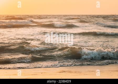 Meeresoberfläche mit schäumenden kleinen Wellen bei Sonnenuntergang. Abendsonne Sonnenschein über dem Meer. Meereswasser Schaum spritzt waschen Sandstrand Stockfoto