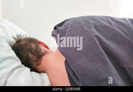 Mann, der morgens unter der Decke im Bett schlief. Rückansicht. Stockfoto