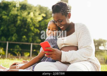 Glückliche, schwanger Mutter und Sohn haben Spaß mit dem Handy im Freien - Fokus auf Mutter Gesicht Stockfoto