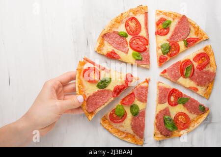 Hand, wobei Scheiben Pizza Margarita. Pizza margarita und Hände Nahaufnahme auf einem hellen Hintergrund. Stockfoto