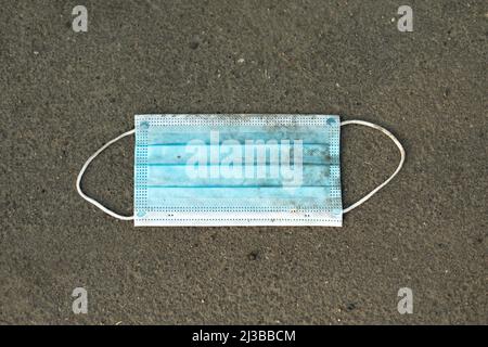 Medizinische Maske auf Asphalt. Verworfene Maske. Müll auf der Straße. Verschmutzung der Umwelt durch medizinische Abfälle. Stockfoto