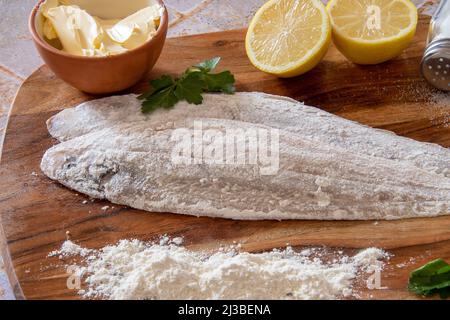 Bemehlter frischer roher Fisch mit Zitronen und Kräutern auf Holzbrett, fertig zum Kochen Stockfoto