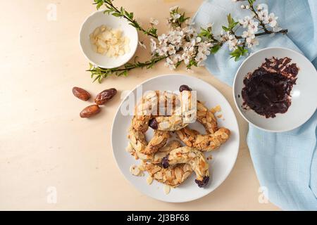 Mandelgebäck ohne Zucker, aber mit Datteln, Haferflocken und dunkler Schokolade, Zutaten und einem Frühlingsblumenzweig auf einem Holztisch, Kopierraum, hoch Stockfoto