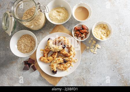 Gesunde Mandel-Halbmond-Kekse ohne Zucker aus Mandeln, Haferflocken und Datteln auf einem Teller und Zutat auf rustikalem grauen Hintergrund, beim Backen Stockfoto