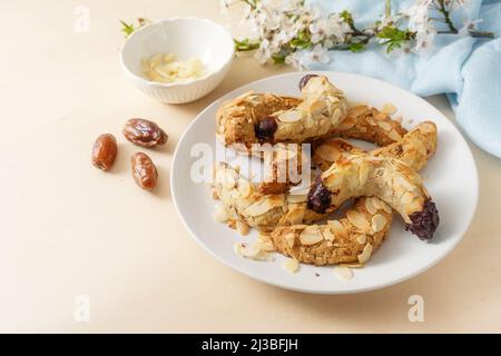 Hausgemachte Kekse aus Mandel, Datteln, Haferflocken und dunkle Schokolade ohne Zucker, Frühlingsblumenzweig und blaue Serviette auf einem Holztisch, Kopierraum, Stockfoto