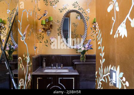 Gold Chinoiserie de Gournay Tapete mit ovalem Spiegel über Waschbecken in Holland Park Home, London, UK Stockfoto