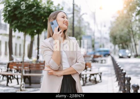 Attraktive junge Frau kommuniziert auf einem Smartphone auf einer Stadtstraße. Stockfoto
