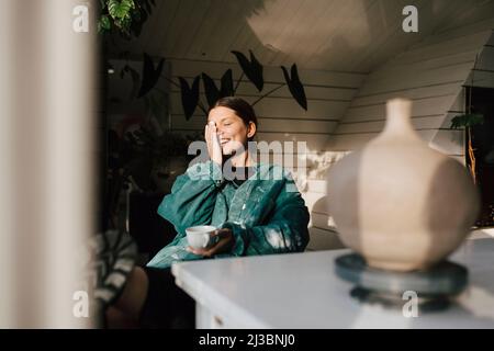 Lächelnde junge Frau mit Kaffee zu Hause Stockfoto