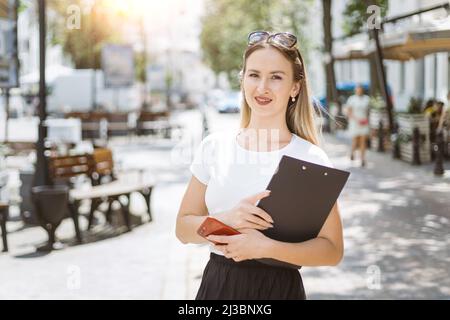 Junge Geschäftsfrau mit einem Ordner mit Dokumenten, die auf einer Stadtstraße stehen. Stockfoto