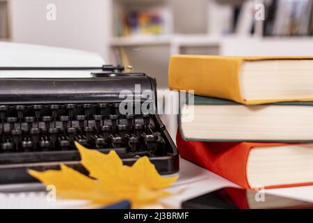 Herbststimmung. Auf dem Tisch stehen alte Schreibmaschine, modernes Mobiltelefon, Bücher, Notizbuch und Stift, trockene gelbe Ahornblätter. Arbeitsplatz des Studenten oder Schriftstellers. Stockfoto