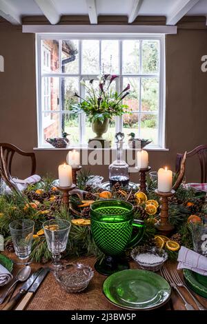 Zündete Kerzen mit orange und Kiefer Mittelpunkt auf Esstisch zu Weihnachten in 18. Jahrhundert Suffolk Cottage, Großbritannien Stockfoto