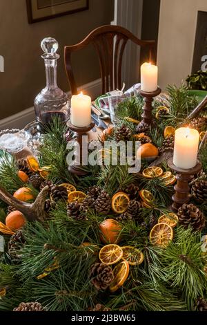 Zündete Kerzen mit aufgeschnittenem Orange und Pinecon-Mittelpunkt auf dem Esstisch zu Weihnachten in Suffolk Cottage aus dem 18.. Jahrhundert, Großbritannien Stockfoto