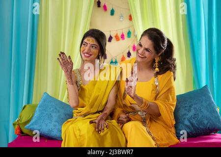 Mutter und Tochter zeigen auf der Haldi-Zeremonie ihre Handflächen mit Mehndi malen Stockfoto