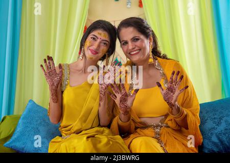 Mutter und Tochter zeigen auf der Haldi-Zeremonie ihre Handflächen mit Mehndi malen Stockfoto