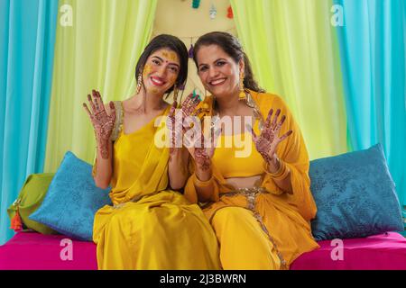 Mutter und Tochter zeigen auf der Haldi-Zeremonie ihre Handflächen mit Mehndi malen Stockfoto