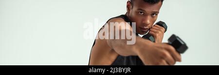 Perfekte Muskeln. Muskulöser junger afrikanischer Mann, der mit Hanteln trainiert, während er vor grauem Hintergrund steht Stockfoto
