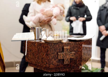 Katholische Kindertaufen. Eine Mutter hält ihr Baby über einem Brunnen in einer katholischen Kirche. Stockfoto