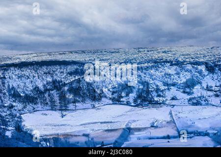 In den kalten Wintermonaten, Blick in ein Tal, mit schneebedeckten Feldern und Hügeln mit Bäumen und einem grauen wolkenübersäten Himmel, Nidderdale, Großbritannien. Stockfoto