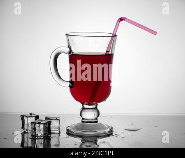 Kalter Tee, Cocktail, Fruchtgetränk in einer hohen Glasschale mit Trinkhalm auf einem Tisch mit Eisstücken auf einem hellgrauen Hintergrund. Sommer dr Stockfoto