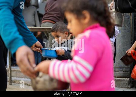 Palästinensische Kinder erhalten Suppentöpfe aus einem Zentrum einer lokalen Wohltätigkeitsorganisation, die während des heiligen Monats Ramadan im Flüchtlingslager Al-Nuseirat im zentralen Gazastreifen kostenlose Mahlzeiten anbietet. Muslime auf der ganzen Welt, vor allem im heiligen Monat Ramadan, bieten eine Menge von Wohltätigkeitsorganisationen wie kostenlose Mahlzeiten Verteilungszentren an, die sie als „Tekeya“ für arme Menschen bezeichnen. (Foto von Ahmed Zakot / SOPA Images/Sipa USA) Stockfoto