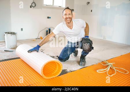 Ein Arbeiter installiert eine orangefarbene Membranabdichtung auf dem Boden Stockfoto