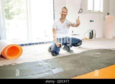 Ein Arbeiter installiert eine orangefarbene Membranabdichtung auf dem Boden Stockfoto