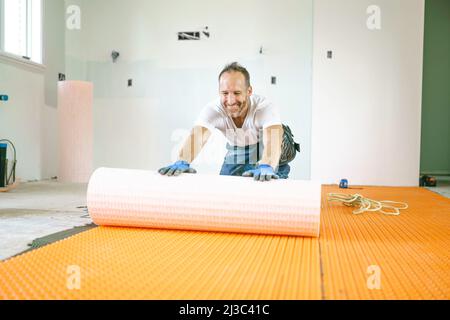 Ein Arbeiter installiert eine orangefarbene Membranabdichtung auf dem Boden Stockfoto