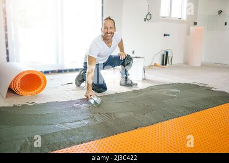 Ein Arbeiter installiert eine orangefarbene Membranabdichtung auf dem Boden Stockfoto