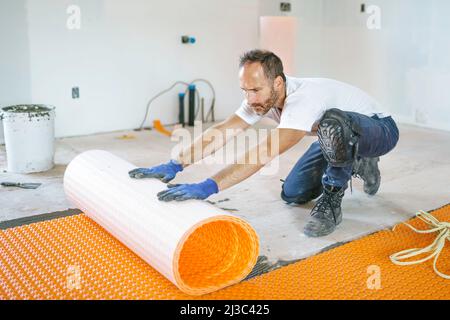 Ein Arbeiter installiert eine orangefarbene Membranabdichtung auf dem Boden Stockfoto