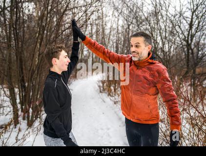 Vater mit Sohn Sport läuft zusammen draußen in der Wintersaison tun High Five Stockfoto