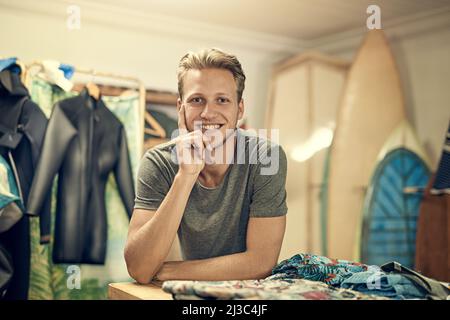 Ich habe alle Surfausrüstung, die man braucht. Porträt eines jungen Ladenbesitzers, der in seinem Surf-Shop posiert. Stockfoto