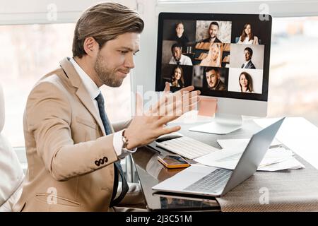 Aufgeregter kaukasischer Mann, der seine Hände überrascht in der Nähe des Gesichts hält, im Büro am Schreibtisch sitzen, sich mit den Arbeitsnachrichten überglücklich fühlen, überglücklich mailen Männer am Laptop, Stockfoto