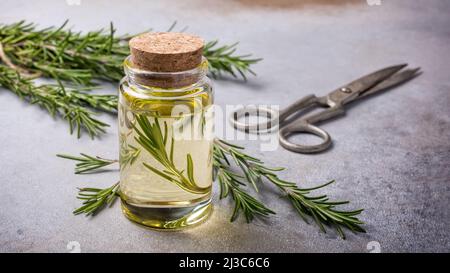 Glas Olivenöl mit Küchenkräutern grünem Rosmarin für gesunde Ernährung auf grauem Betongrund Stockfoto