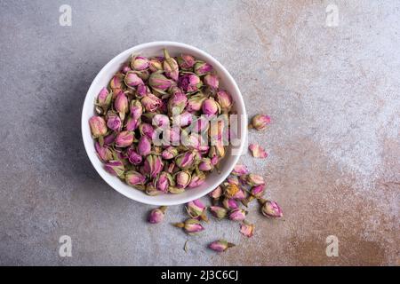Draufsicht auf weiße Schale mit getrockneten Rosenknospen für duftenden Tee auf grauem Betongrund Stockfoto