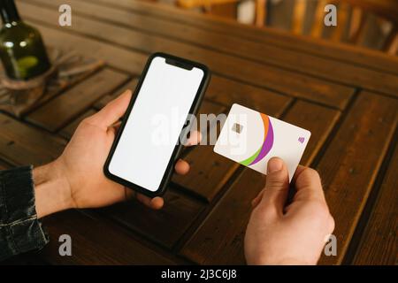 Junger Mann, der in einem Café mit Kreditkarte und Telefon in den Händen sitzt und beim Online-Shopping Einkäufe tätigt. Online-Zahlung. Mann hält Smartphone mit BL Stockfoto