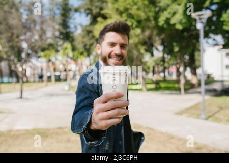 Posiert, junger Mann hält Kaffeebecher und lächelt, Kaffee Spaß und Park Stockfoto