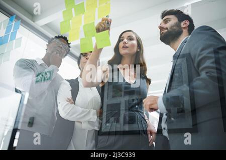 Sie sind entschlossen, nur die besten Ideen zu entwickeln. Eine kurze Aufnahme von Kollegen beim Brainstorming mit Haftnotizen an einer Glaswand in einem modernen Büro. Stockfoto