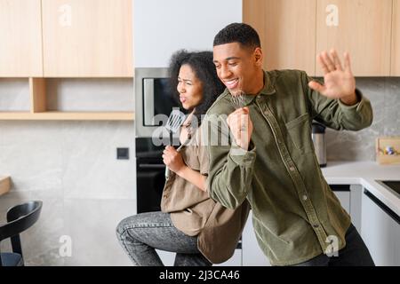 Ein hübscher Mann und eine attraktive junge Frau kochen und haben Spaß zusammen, während sie Zeit in der Küche verbringen. Romantisches interrassisches Paar tanzt beim Zubereiten von Mittag- oder Abendessen Stockfoto