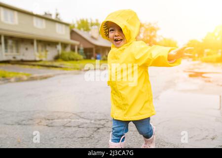 Lustige niedliche Baby-Mädchen tragen gelben wasserdichten Mantel und Stiefel spielen im Regen Stockfoto