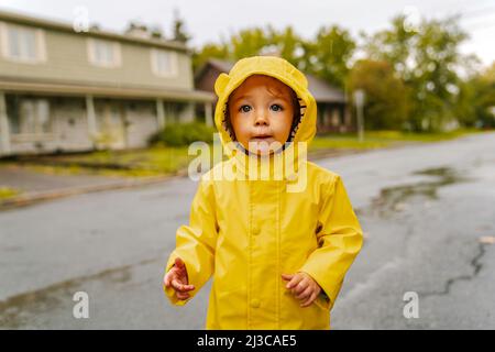 Lustige niedliche Baby-Mädchen tragen gelben wasserdichten Mantel und Stiefel spielen im Regen Stockfoto