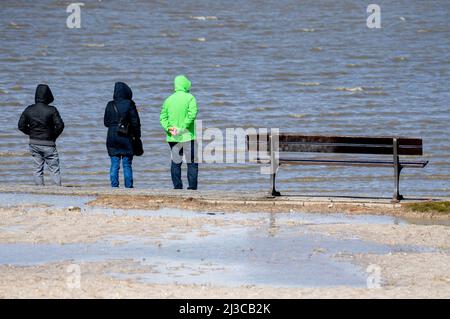 Harlesiel, Deutschland. 07. April 2022. Touristen stehen bei stürmischem Wetter am Strand und blicken über die Nordsee. Der Deutsche Wetterdienst (DWD) warnt vor Stürmen, Gewittern und Starkregen in Niedersachsen. Quelle: Hauke-Christian Dittrich/dpa/Alamy Live News Stockfoto