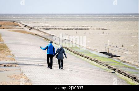 Harlesiel, Deutschland. 07. April 2022. Bei stürmischem Wetter laufen Touristen an der Strandpromenade vor der Nordsee entlang. Der Deutsche Wetterdienst (DWD) warnt vor Stürmen, Gewittern und Starkregen in Niedersachsen. Quelle: Hauke-Christian Dittrich/dpa/Alamy Live News Stockfoto