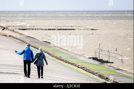 Harlesiel, Deutschland. 07. April 2022. Bei stürmischem Wetter laufen Touristen an der Strandpromenade vor der Nordsee entlang. Der Deutsche Wetterdienst (DWD) warnt vor Stürmen, Gewittern und Starkregen in Niedersachsen. Quelle: Hauke-Christian Dittrich/dpa/Alamy Live News Stockfoto