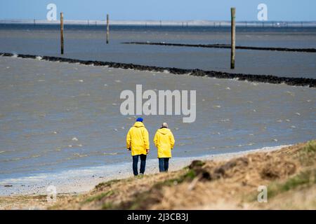 Harlesiel, Deutschland. 07. April 2022. Bei stürmischem Wetter spazieren Touristen am Strand entlang und blicken auf die Nordsee. Der Deutsche Wetterdienst (DWD) warnt vor Stürmen, Gewittern und Starkregen in Niedersachsen. Quelle: Hauke-Christian Dittrich/dpa/Alamy Live News Stockfoto