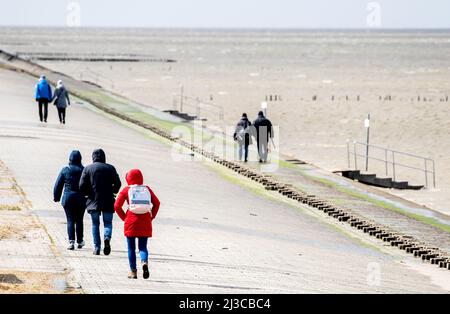 Harlesiel, Deutschland. 07. April 2022. Bei stürmischem Wetter laufen Touristen an der Strandpromenade an der Nordsee entlang. Der Deutsche Wetterdienst (DWD) warnt vor Stürmen, Gewittern und Starkregen in Niedersachsen. Quelle: Hauke-Christian Dittrich/dpa/Alamy Live News Stockfoto