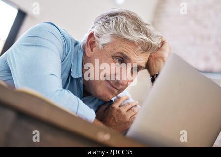 Ich kann kaum zuschauen. Aufnahme eines reifen Mannes, der alleine sitzt und sich gestresst fühlt, während er seinen Laptop von zu Hause aus verwendet. Stockfoto