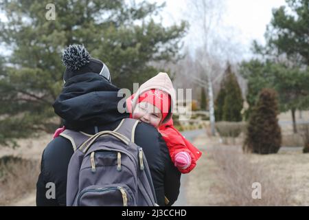 Kleines lustiges Mädchen auf den Armen des Vaters. Tochter umarmt Vater. Vater hält Tochter im Freien Stockfoto